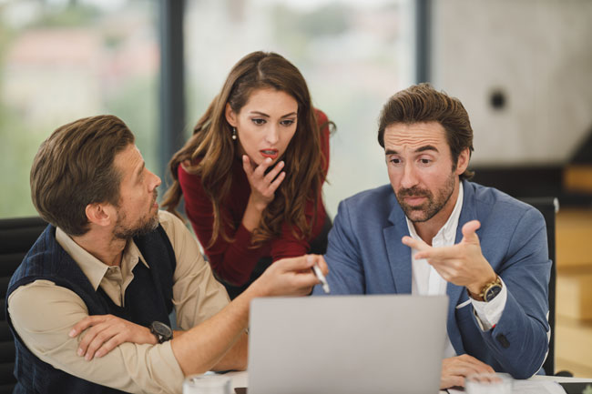 Equipo comercial de tres personas conversando sobre lo que muestra el portátil